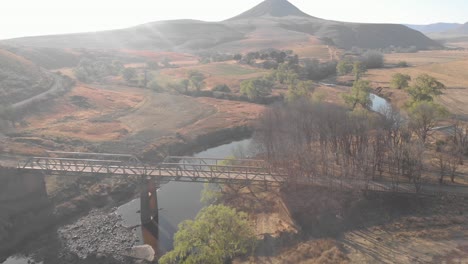 Luftverfolgung-Eines-Mountainbikers,-Der-Eine-Stahlbrücke-Auf-Einer-Schotterstraße-überquert