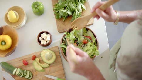 mujer caucásica madura preparando ensalada, añadiendo verduras