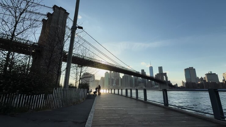 Il sole si riflette sull'acqua sotto il Ponte di Brooklyn, che porta a Manhattan, dal punto di vista di qualcuno seduto sulla passerella sul lato di Dumbo, Brooklyn.
