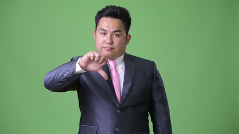 young handsome overweight asian businessman against green background