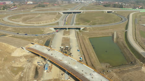 Vista-Aérea-De-Un-Cruce-De-Carreteras-En-Construcción-Con-Maquinaria-Pesada-Y-Un-Estanque.