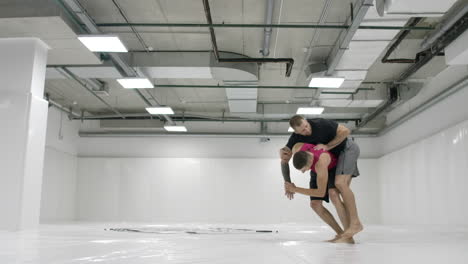 dos luchadores masculinos en una habitación blanca trabajan lanzando esteras. toma un agarre y lanza a través de ti mismo.