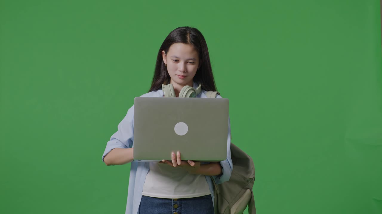 초록색 스크린 배경 스튜디오에 서 있는 동안 을 사용하고 을 가리키는 뒷면을 가진 아시아 소녀 학생