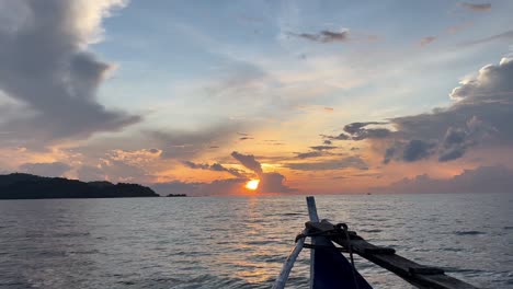 Un-Barco-Se-Desliza-Serenamente-Hacia-Una-Isla,-Mientras-El-Sol-Se-Eleva-En-El-Horizonte,-Proyectando-Un-Cálido-Resplandor-Sobre-Las-Tranquilas-Aguas