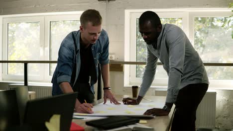 Two-Business-Partners-Are-Working-Together,-Brainstorming,-Pointing-At-The-Table-With-Yellow-Papers-On-It-With-The-Pencils-On-Business-Meeting