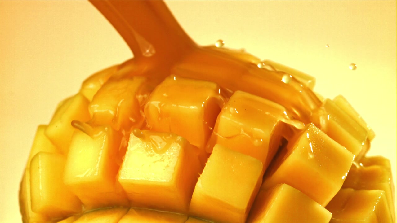 Sciroppo dorato che cola su mango fresco a cubetti al rallentatore
