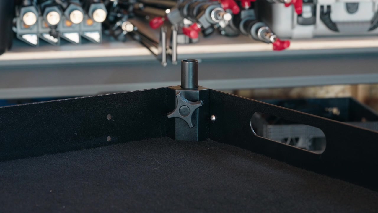Primo piano di un supporto angolare per carrello della telecamera dotato di una manopola di regolazione, con accessori fotografici visibili sullo sfondo