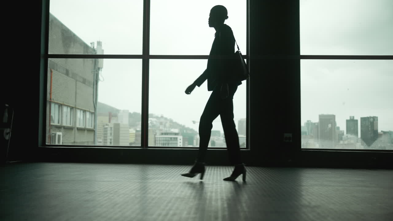 Silhouette of a woman walking by a window overlooking a cityscape
