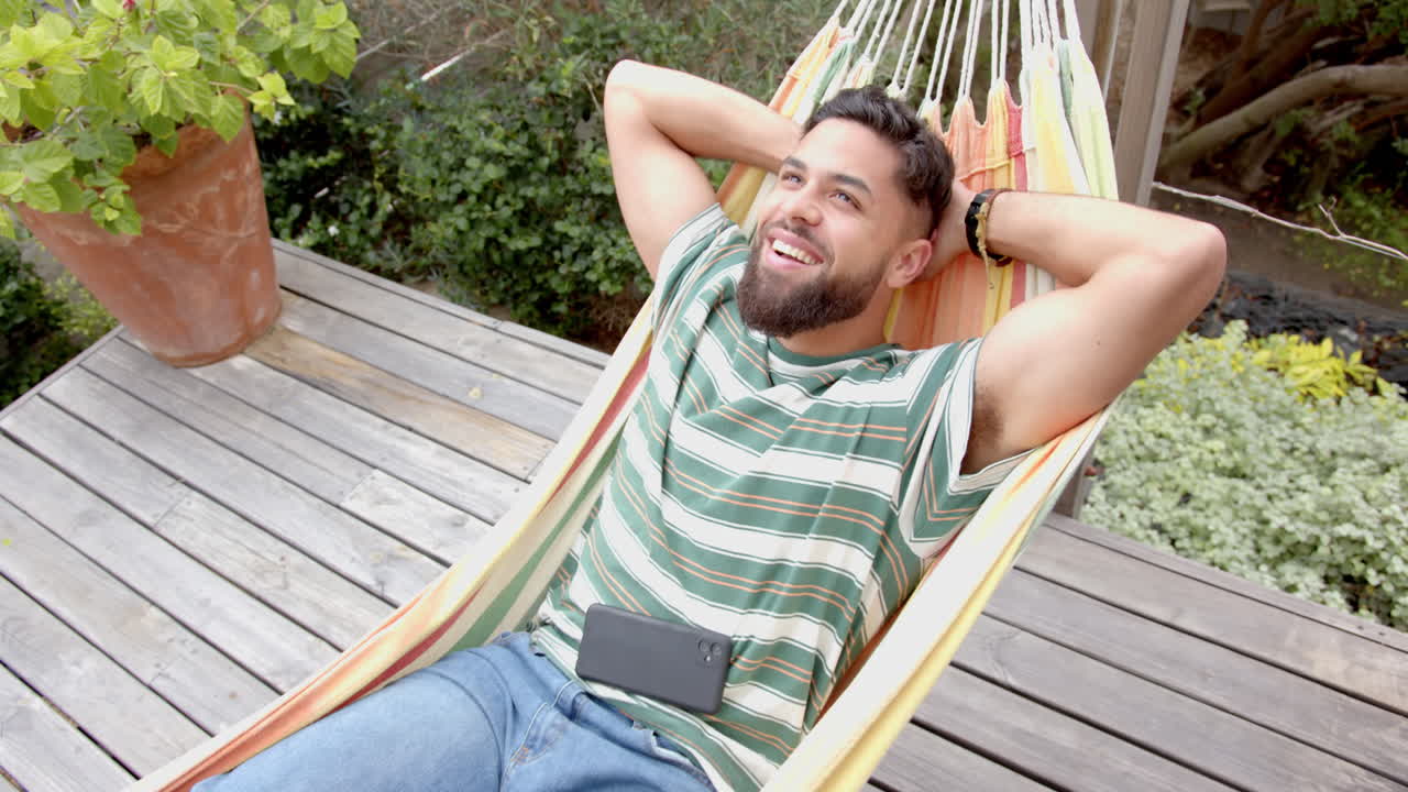 Relaxing in hammock, man smiling with smartphone on lap, enjoying leisure time