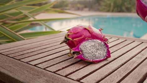 man takes a piece of dragon fruit with a swimming pool in the background