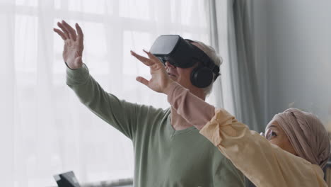 mujer árabe de mediana edad ayudando a un anciano feliz a usar gafas de realidad virtual en casa 1