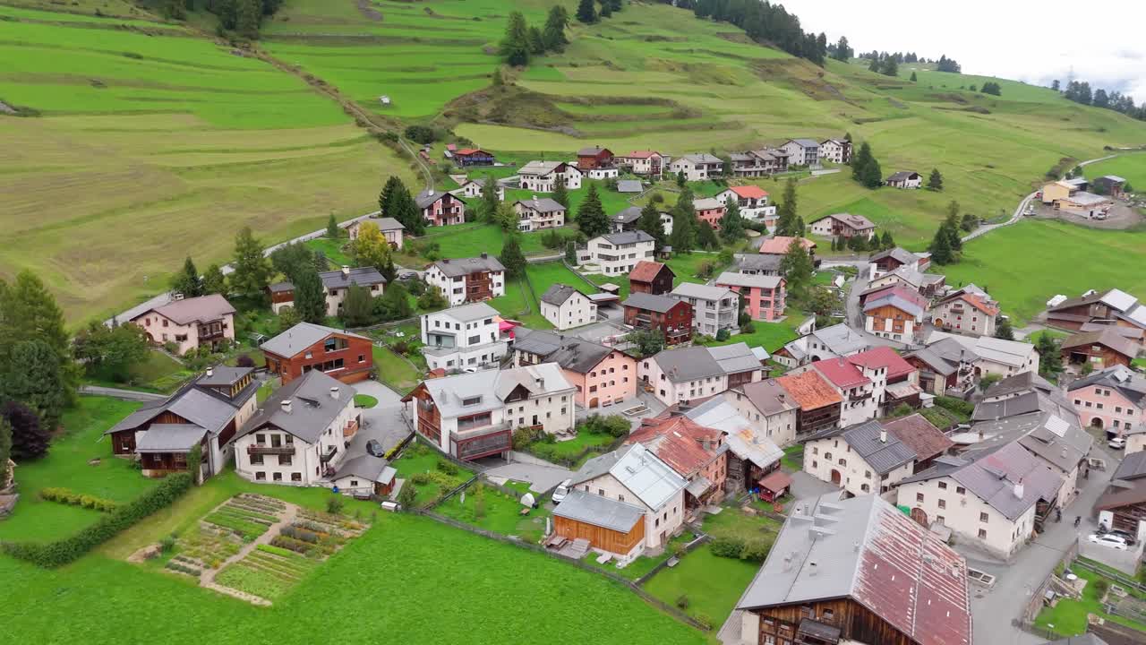 Aerial view of Ftan village in Switzerland with traditional alpine houses, green meadows and scenic mountain landscape. Peaceful serene landscape in summer. Top down