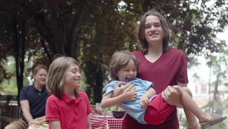 handheld shot of three brothers having fun and looking at the camera during a family picnic in the forest