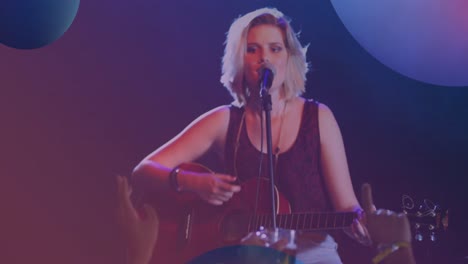 animation of spheres over caucasian woman playing acoustic guitar and singing into microphone