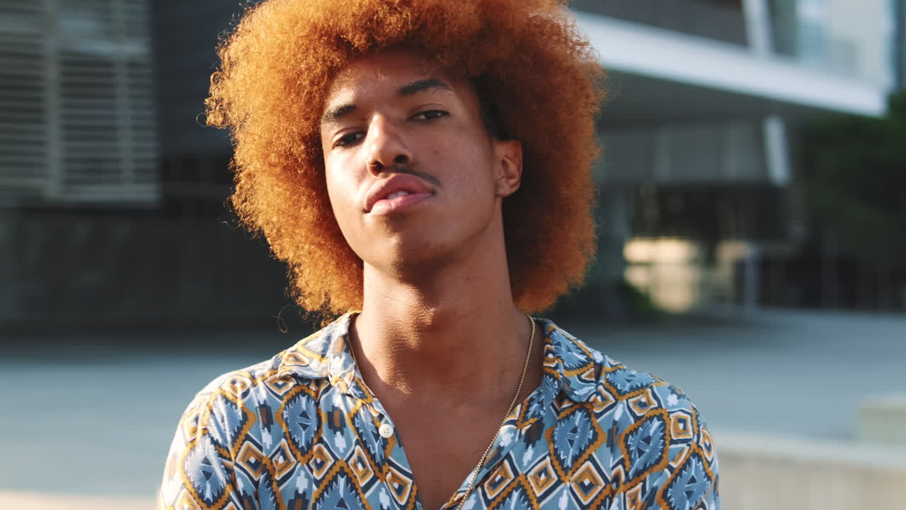 Confident Young Man with Red Afro Hair Posing in Urban Setting