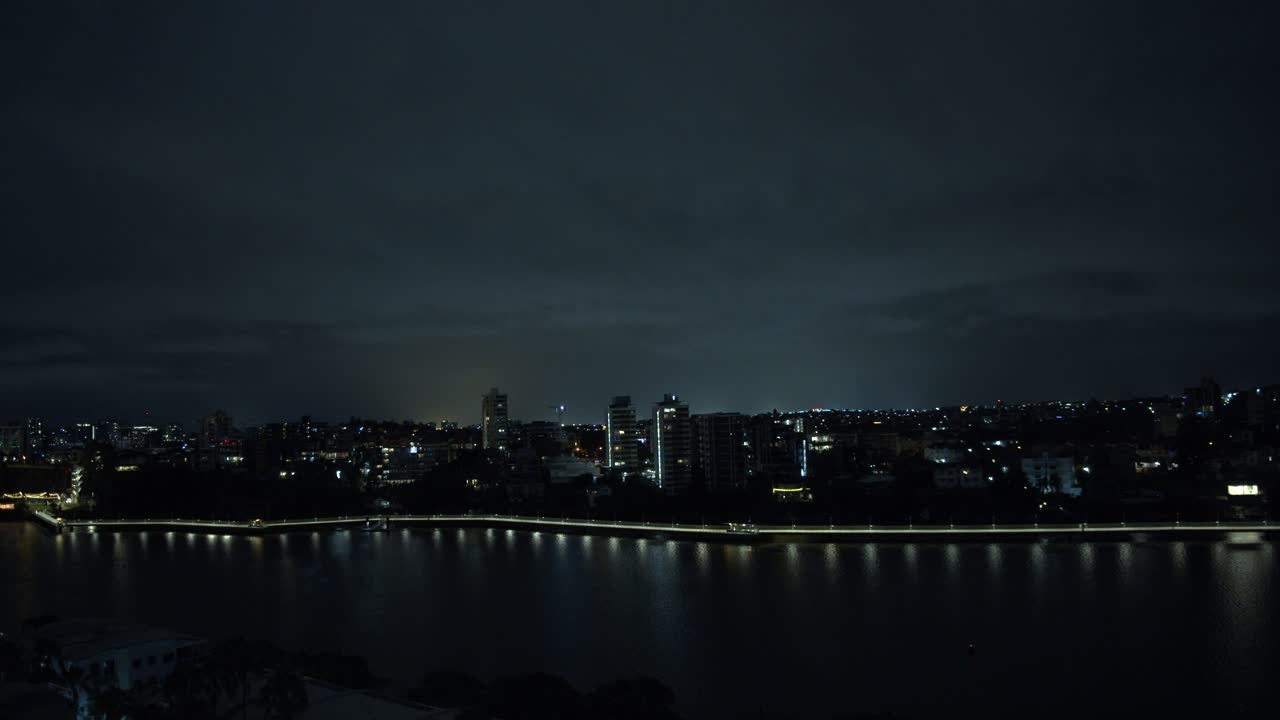 A small city with medium sized apartment buildings is alive and active as its lights spill onto a busy river where boats fly past at every moment