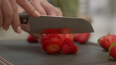 a close-up of a woman's hands slicing a ripe, red strawberry on a cutting board