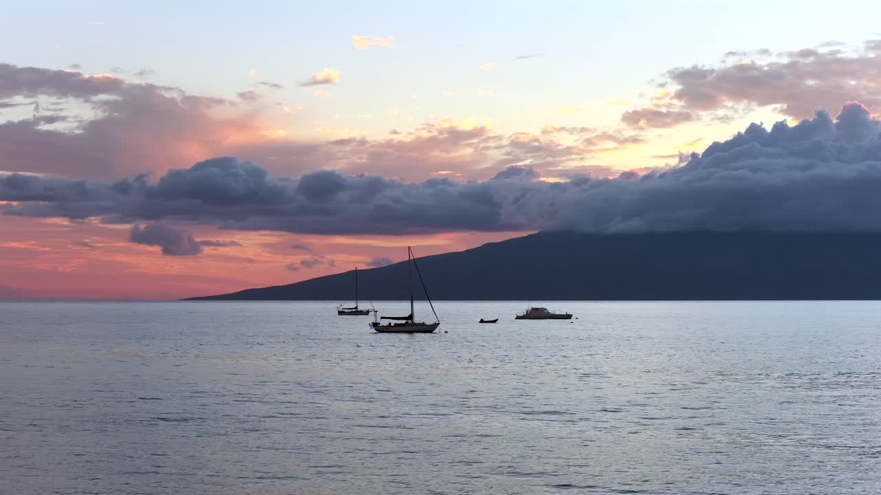 A tranquil coastal view off Lahaina, Maui, with fishing boats drifting across calm evening waters and the island of Lānaʻi silhouetted beneath colorful sunset clouds