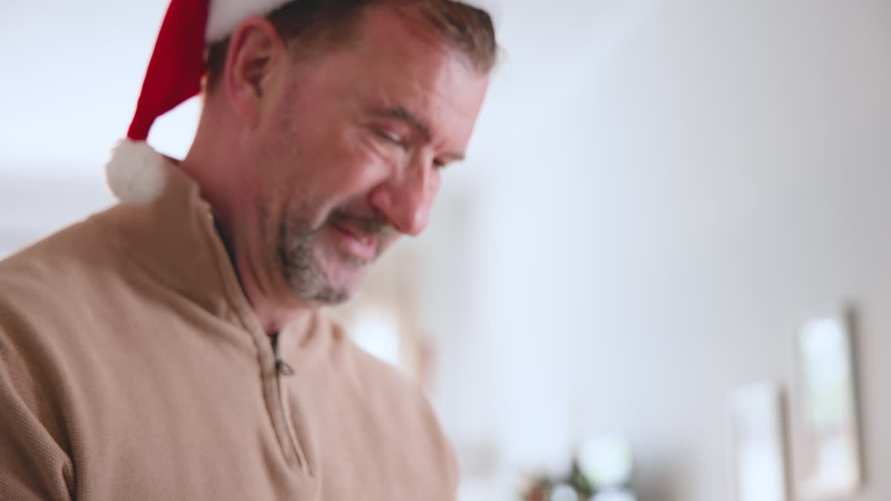 At Christmas, Smiling senior man wearing Santa hat enjoying festive holiday at home