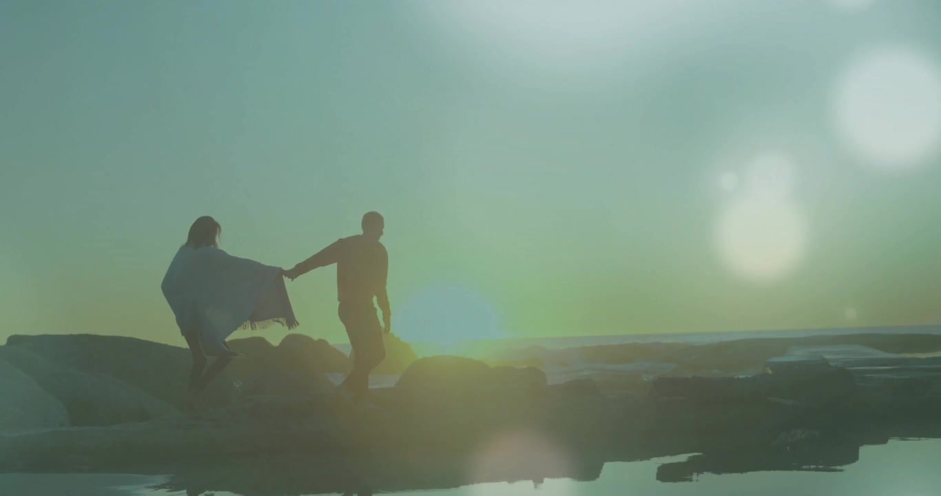 Couple Holding Hands Walking on Rocky Beach at Sunset