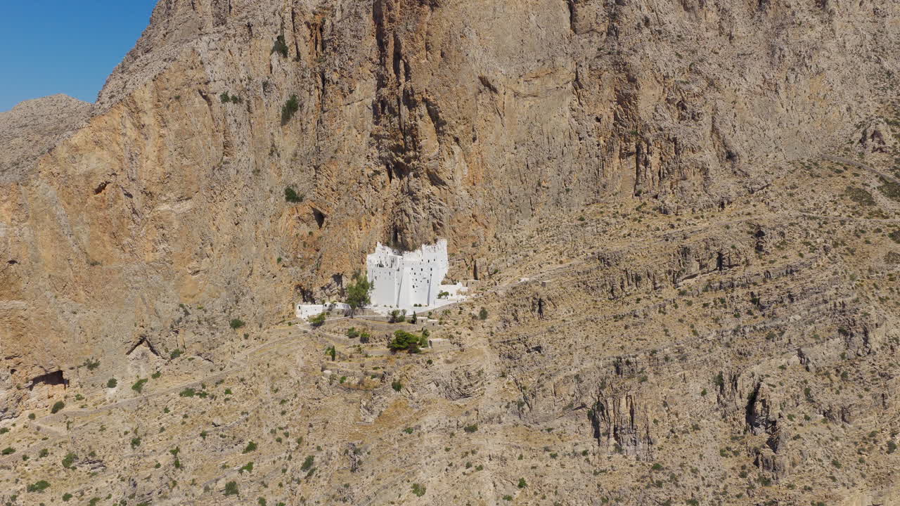 Drone footage showcasing the stunning Chozoviotissa Monastery in Amorgos, with whitewashed walls reflecting the strong noon sunlight above the Aegean Sea
