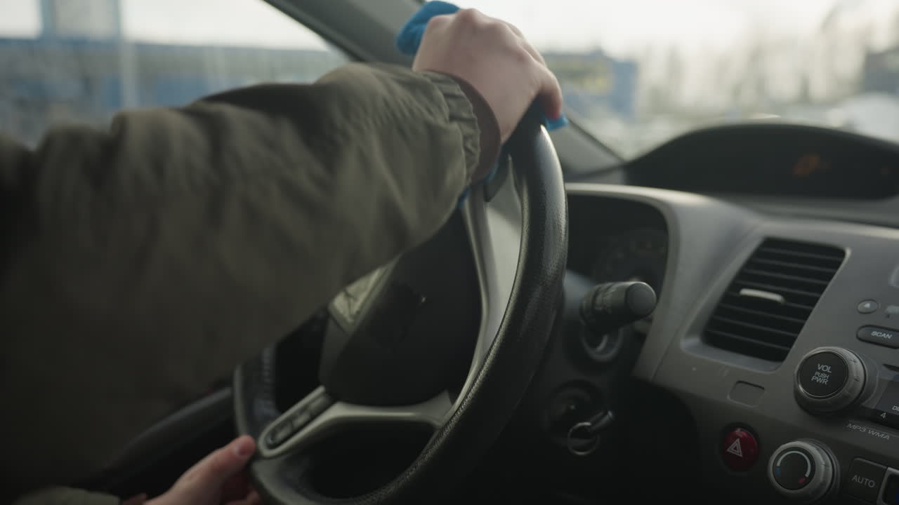 driver cleaning steering wheel with blue rag inside car cabin close up shot showing cloth wiping leather wheel for maintenance detailing and hygiene routine before winter drive