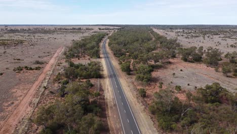 Drohne-Fliegt-über-Versiegelte-Straße-Und-Eine-Eisenbahnlinie-In-Einer-Wüstenlandschaft-Im-Australischen-Outback