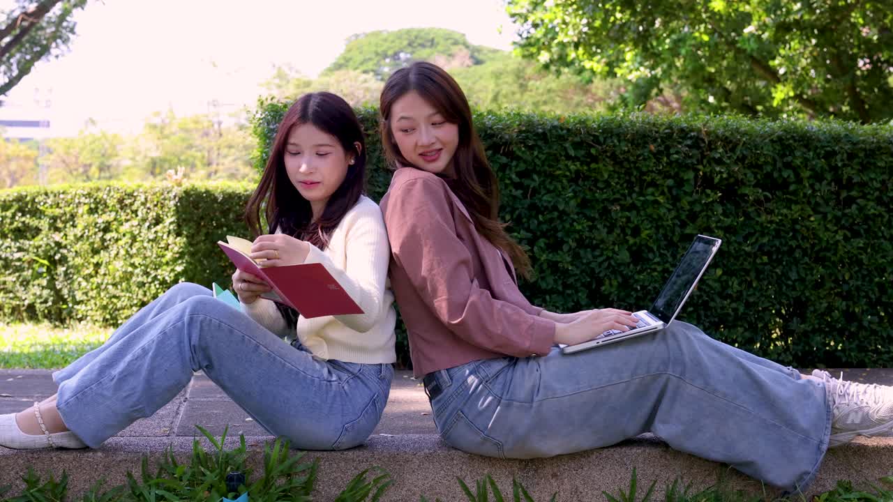 2人の女子学生が、屋外で自然光の中、背中合わせに座ってノートパソコンとノートブックを使っている。