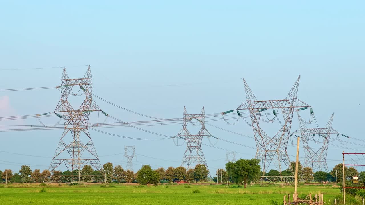A detailed view of high-voltage transmission towers with glass insulators spanning across green farmland under a clear blue sky — perfect for educational videos documentaries