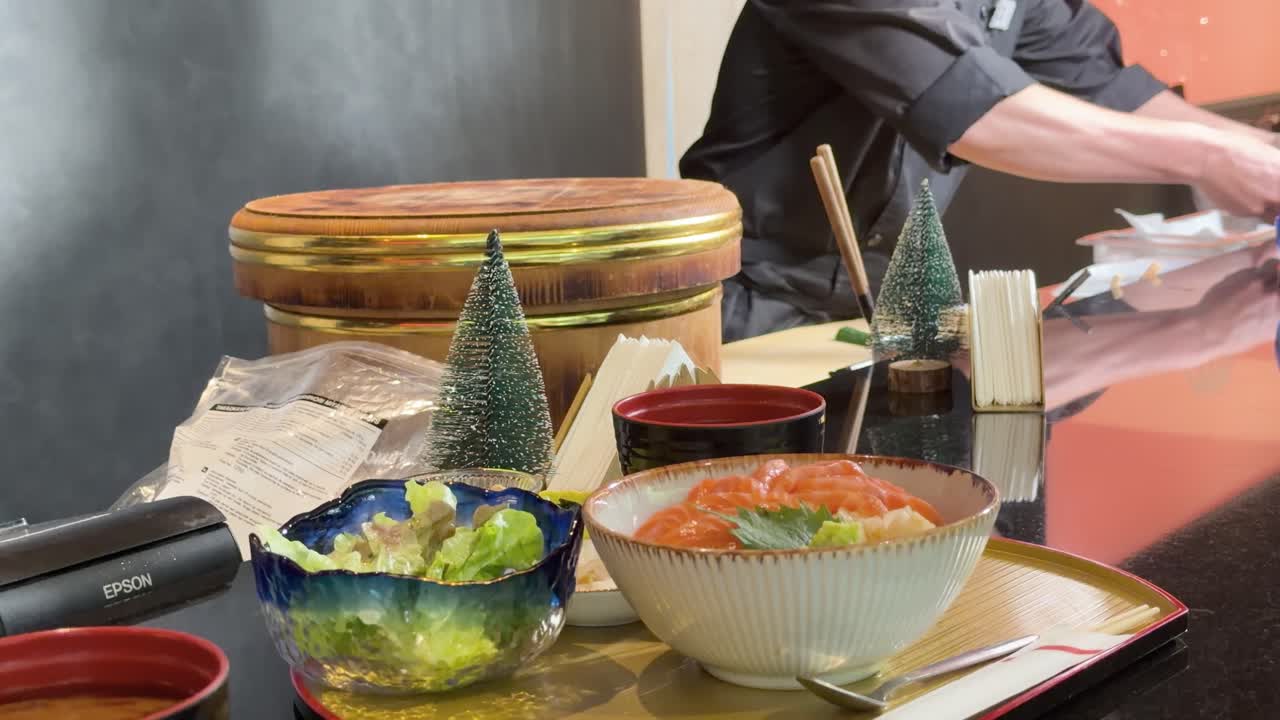 Close-up of Japanese chef serving salmon rice bowl at restaurant counter with warm lighting