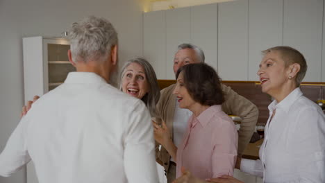 Group-Of-Cheerful-Senior-Friends-Greeting-Each-Other-With-Hugs-In-The-Kitchen-2