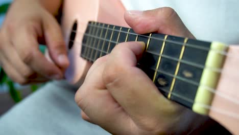 hombre de mediana edad 30 y con cuentas está jugando y silbando con su ukulele rosado al lado de una gran ventana y cerca de una planta verde