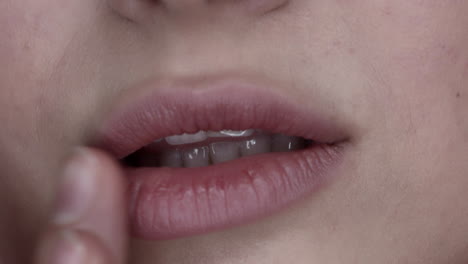 closeup of the firm lips of a young woman gently touching her lips with a finger to pat the cosmetic