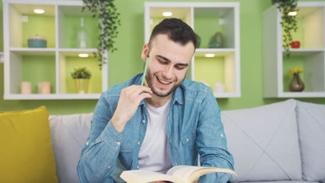 un joven feliz y sonriente leyendo un libro en casa soñando despierto.