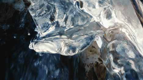 drop falling on icicle in a frozen river in winter with flowing water, close up, slow motion