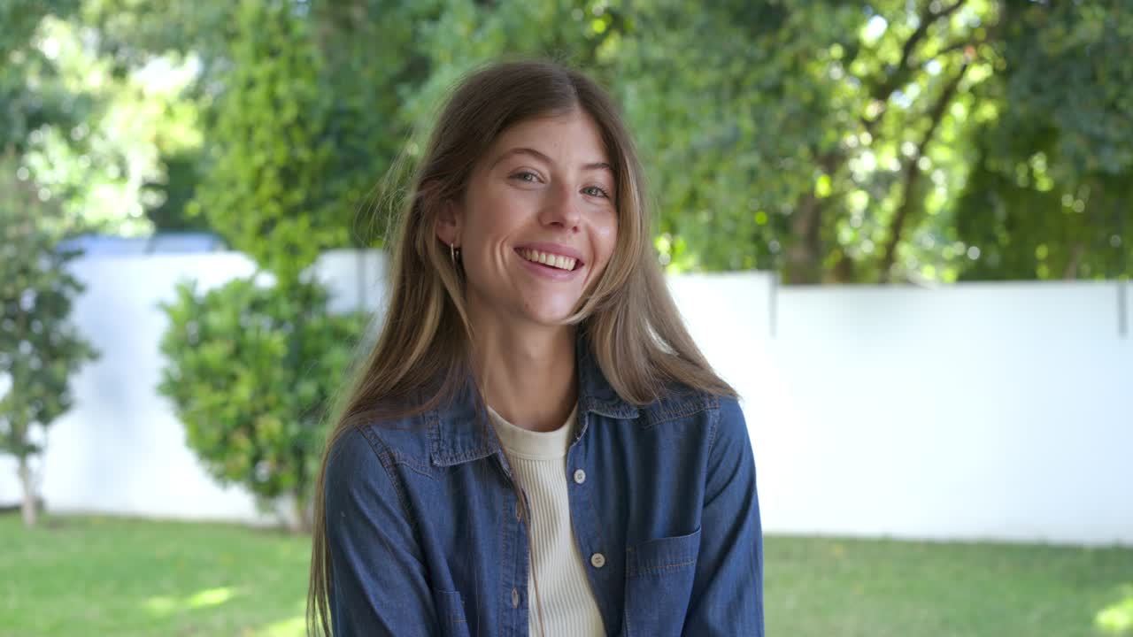 Mujer que se da cuenta del cable de los auriculares, se ajusta la camisa vaquera, levanta la cabeza y posa en el porche para un retrato