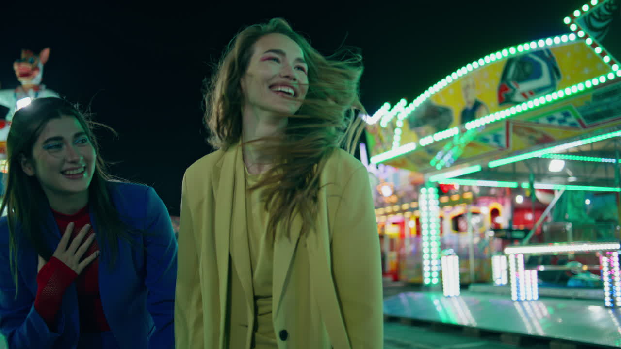 Cheerful friends having fun at night amusement park. Happy girls laughing walk