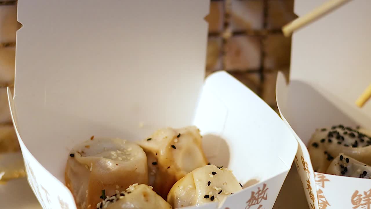 Chopsticks lifting buns from a takeout box