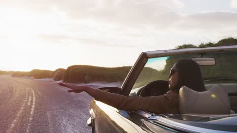 African-american-woman-driving-along-country-road-in-convertible-car