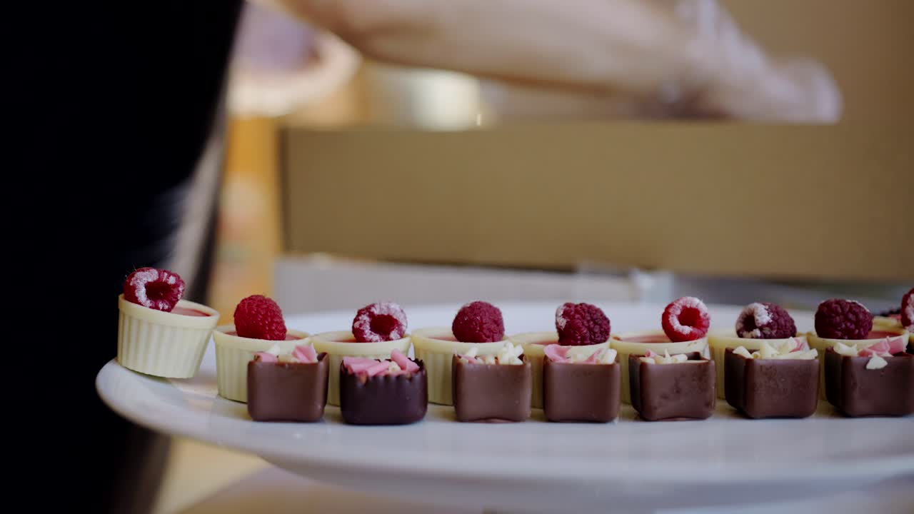 Hånd med plasthandske placerer chokolade- og bær-søde sager på tallerken, nærbillede.