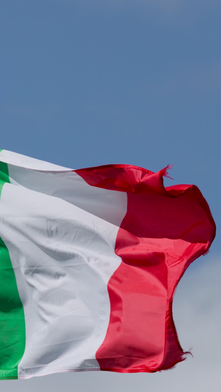Bandiera tricolore italiana che sventola dinamicamente all'aperto, con luce del giorno intensa e cielo azzurro limpido, vista ravvicinata.