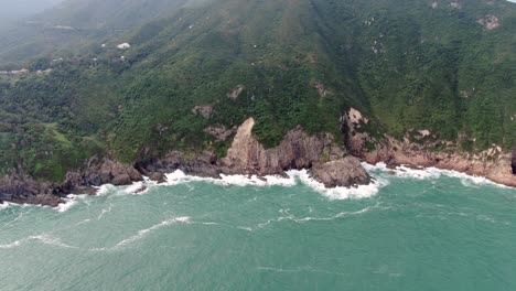 Aerial-view-of-a-jagged-rock-island,-surrounded-with-lush-green-nature-and-Hong-Kong-bay-water