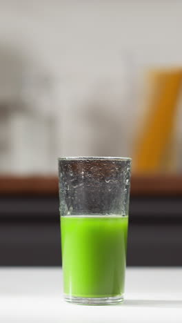 vaso medio lleno de jugo de pasto de trigo verde vibrante en un mostrador de cocina blanco, fondo borroso