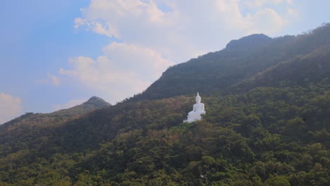 luang por khao, wat theppitak punnaram, aerial 4k footage towards the giant white buddha statue on a mountain side in pak chong, thailand, in the afternoon, blue cloudy sky, birds flying around