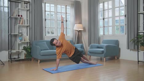 hombre asiático haciendo yoga en postura de tabla lateral en la alfombra en casa