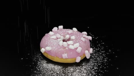 tasty fresh donut lay on black surface and gets sprinkle with icing sugar powder