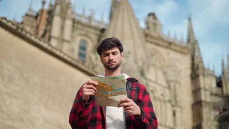 hipster tourist examining map near old building