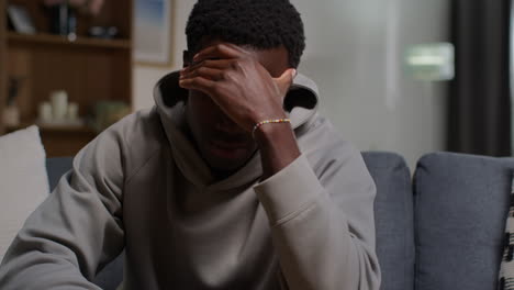 close up of unhappy and depressed young man with head in hands sitting on sofa at home shaking head 1