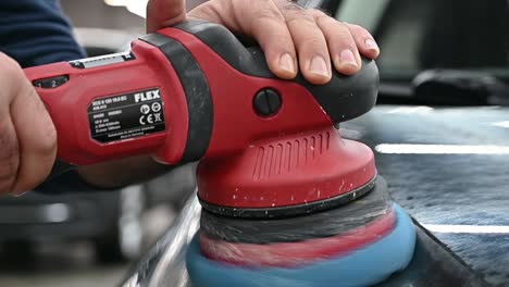 Polishing-black-vehicle-hood-with-industrial-tool,-close-up-slow-motion-shot