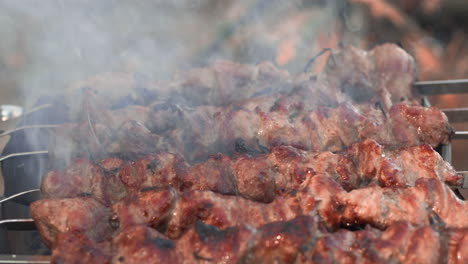 Closeup-smoked-bbq-flipping-over-charcoal.-Pork-kebabs-cooking-on-grill-outdoor